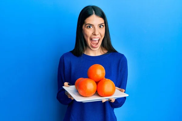 Jovem Hispânica Segurando Prato Com Laranjas Frescas Comemorando Louco Espantado — Fotografia de Stock