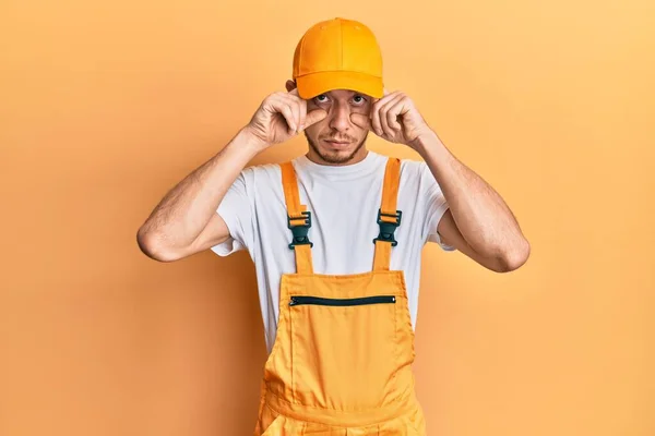 Hispanic Young Man Wearing Handyman Uniform Trying Open Eyes Fingers — Zdjęcie stockowe
