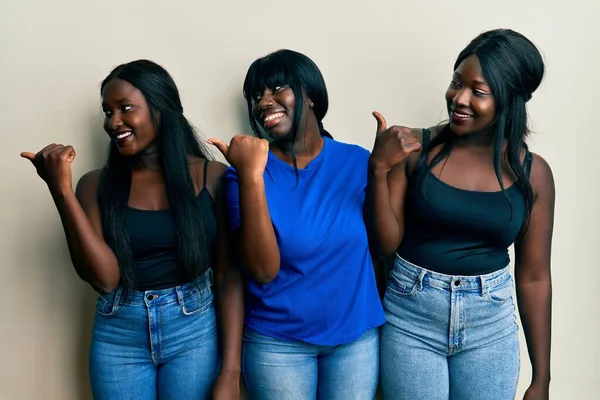 3人の若いアフリカ系アメリカ人の友人を着てカジュアルな服を指差す親指で側に笑顔で幸せなオープン口 — ストック写真