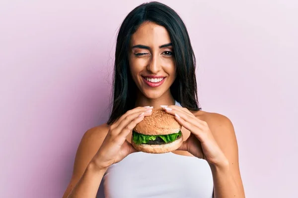 Beautiful Hispanic Woman Eating Tasty Classic Burger Winking Looking Camera — Stockfoto