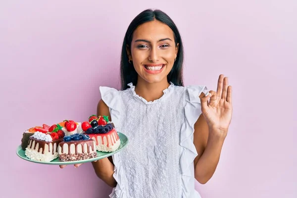 Young Brunette Woman Holding Cake Slices Doing Sign Fingers Smiling — Fotografia de Stock
