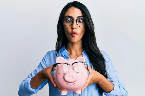 Beautiful Hispanic Woman Holding Piggy Bank Glasses Making Fish Face — 스톡 사진
