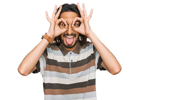 若いヒスパニック系の男性は 双眼鏡の舌を突き出すような をジェスチャーを行うカジュアルな服を着て 目の指を見て クレイジーな表現 — ストック写真