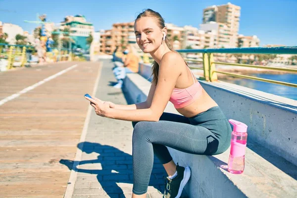 Mladá Blondýna Sportovkyně Dělá Cvičení Pomocí Smartphone Sedí Lavičce Promenádě — Stock fotografie