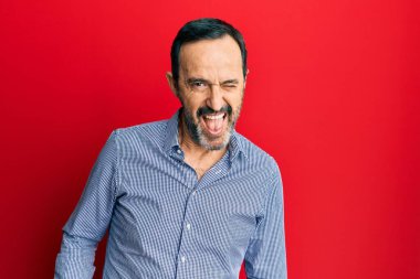 Orta yaşlı İspanyol bir adam, sıradan kıyafetler giymiş, kameraya seksi bir ifadeyle bakıyor, neşeli ve mutlu bir yüzle.. 