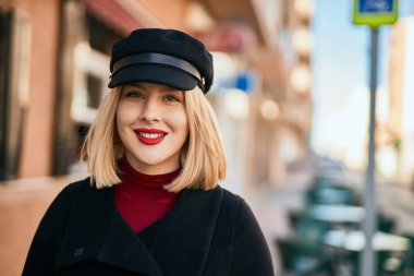 Genç sarışın kadın gülümsüyor, mutlu bir şekilde şehirde duruyor..