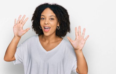 Genç Afro-Amerikan kızı gündelik giysiler giyip on numarayı gösterirken kendinden emin ve mutlu bir şekilde gülümsüyor.. 