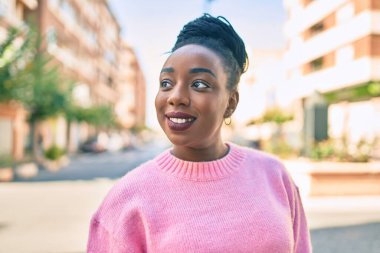 Genç Afrikalı Amerikalı kadın gülümseyerek şehirde mutlu mesut yürüyor..