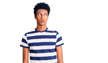 Genç Afro-Amerikan adam günlük kıyafetler giyiyor gülümsüyor yan tarafa bakıyor ve düşünüyor. 