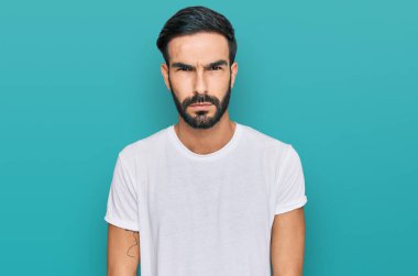 Gündelik beyaz tişört giyen, kuşkucu ve gergin genç İspanyol adam sorun yüzünden surat asıyor. negatif kişi. 