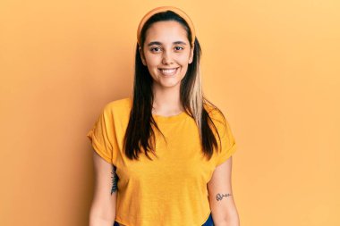 Yüzünde mutlu ve havalı bir gülümseme olan günlük sarı tişört giyen genç İspanyol kadın. şanslı kişi. 