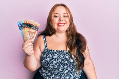 Ayrıca Kanada doları tutan beyaz bir kadın. Pozitif ve mutlu görünüyor. Dişlerini gösteren bir gülümsemeyle ayakta duruyor. 