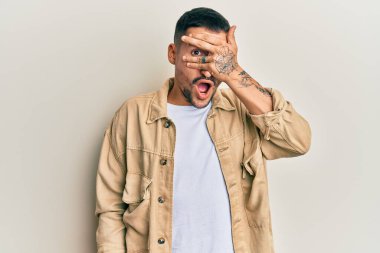 Dövmeleri olan yakışıklı bir adam günlük kahverengi kot ceket giyiyor. Şoka girip yüzünü ve gözlerini eliyle kapatıyor. Utanmış bir ifadeyle parmaklarından bakıyor.. 