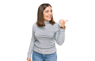 Balıkçı yaka kazak giyen, gülümseyen, gülümseyen ve baş parmağıyla yan tarafı gösteren genç ve güzel bir kadın.. 