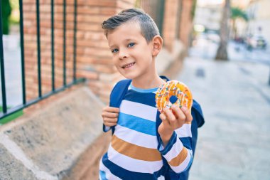 Sevimli beyaz çocuk gülümsüyor. Mutlu bir şekilde şehirde donut yiyor..