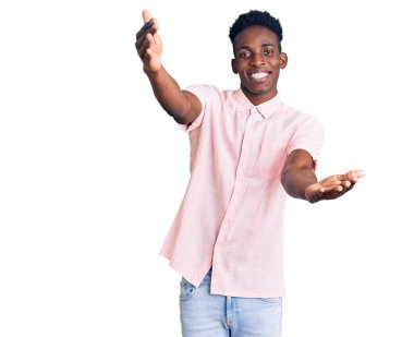 Gündelik giysiler giymiş genç Afro-Amerikan bir adam kameraya sarılıp gülümseyerek bakıyor. Mutluluğu kucaklayan neşeli bir ifade.. 