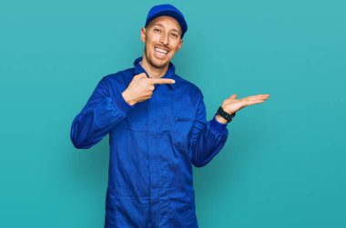 Sakallı, inşaatçı kıyafeti giyen kel adam kameraya hayret ediyor ve gülümsüyor.. 