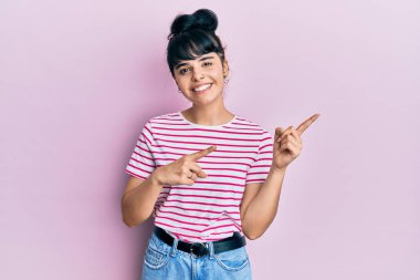 Gündelik kıyafetler giyen, gülümseyen ve kameraya bakan genç İspanyol kız iki eliyle ve parmaklarıyla kenarı işaret ediyor.. 