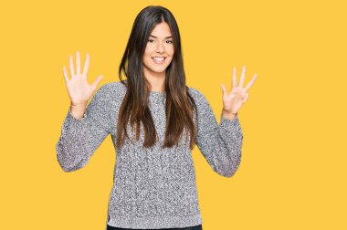 Kış süveteri giyen genç esmer kadın dokuz numarayı gösterip işaret ederken kendine güvenen ve mutlu bir şekilde gülümsüyor.. 