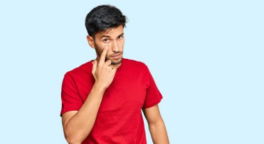 Kırmızı tişört giyen genç yakışıklı adam, senin jestini izlerken, şüpheli bir ifade takınıyor. 