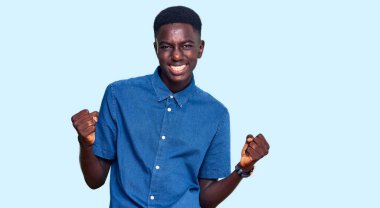 Genç Afro-Amerikan erkeği, gündelik giysiler içinde çok mutlu ve heyecanlı bir şekilde kolları havada, gülümseyerek ve başarı için çığlık atarak kazanan bir jest yapıyor. kutlama konsepti. 