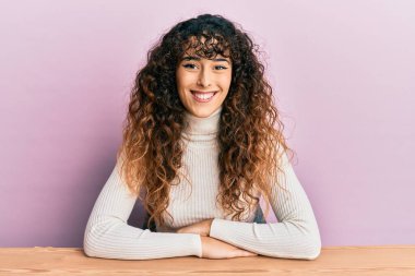 Yüzünde mutlu ve havalı bir gülümsemeyle masada oturan gündelik kıyafetler giyen genç İspanyol kız. şanslı kişi. 