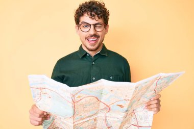 Şehir haritasını tutan kıvırcık saçlı genç beyaz adam kameraya seksi bir ifadeyle bakıyor, neşeli ve mutlu bir yüz.. 
