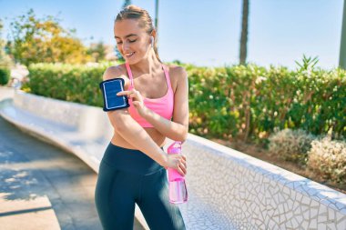 Genç sarışın sporcu şehirde bir şişe su içerek egzersiz yapıyor.