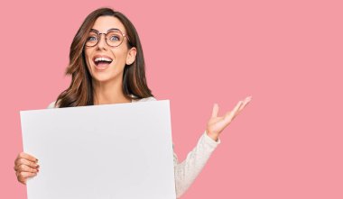 Genç esmer kadın boş afiş tutuyor zaferi mutlu bir gülümsemeyle ve kazanan yüz ifadesiyle kutluyor. 