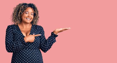 Genç Afro-Amerikan artı cüsseli kadın gündelik giysiler giyip kameraya hayret ediyor ve gülümsüyor.. 