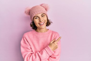 Genç esmer, sevimli yün şapkalı, yüzünde kocaman bir gülümseme olan, eli ve parmağı kameraya bakan bir kadın.. 
