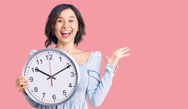 Genç ve güzel bir kız büyük bir saat tutuyor zaferi kutluyor mutlu bir gülümsemeyle ve kazanan bir ifadeyle ellerini kaldırarak 