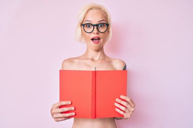 Dövmeli genç sarışın kadın üstsüz bir şekilde kitap okuyor çılgın ve başarıyı kutluyor gözleri açık heyecanla haykırıyor. 