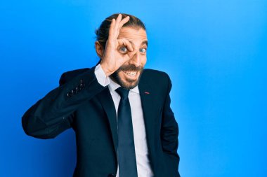 Uzun saçlı, sakallı, takım elbiseli ve kravatlı çekici bir adam mutlu mesut gülümsüyor. 