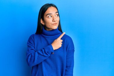 Sıradan bir kazak giyen Asyalı genç bir kadın, elini kaldırmış, ciddi ve sakin bir yüz ifadesi sergiliyor. 