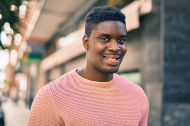 Genç Afrikalı Amerikalı adam gülümseyerek şehirde mutlu mesut duruyor..