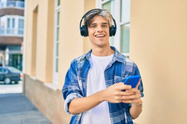 Genç İspanyol adam şehirde akıllı telefon ve kulaklık kullanarak mutlu gülümsüyor..