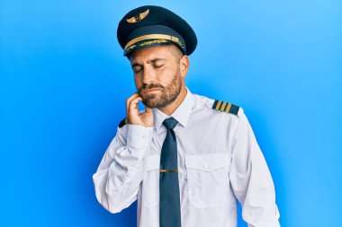 Sakallı, uçak pilotu üniforması giyen yakışıklı diş ağrısı ya da diş hastalığından dolayı ağızlarına acı dolu bir ifadeyle dokunan yakışıklı bir adam. dişçi 