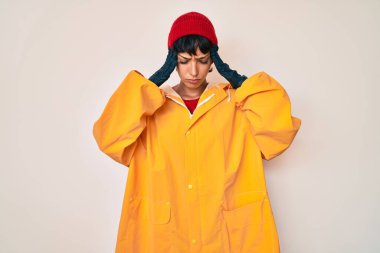 Sarı yağmurluk giyen güzel esmer kadın baş ağrısı çekiyor. Acı ve migren yüzünden çaresiz ve stresli. Eller başının üstünde.. 