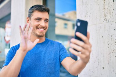 Kafkasyalı genç adam şehirde akıllı telefon kullanarak video araması yaparken mutlu gülümsüyor..