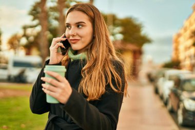 Genç sarışın kız akıllı telefondan konuşuyor. Şehirde kahve içiyor..