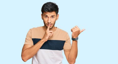 Gündelik giysiler giymiş genç yakışıklı adam sessiz olmak istiyor. Parmakları dudaklarında ve elleri yandan işaret ediyor. sessizlik ve gizli konsept. 