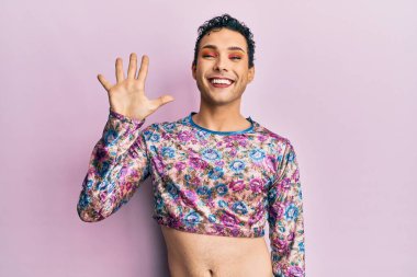 Makyaj giysileri giymiş yakışıklı bir adam beş numarayı gösterip işaret ederken kendinden emin ve mutlu gülümsüyor.. 