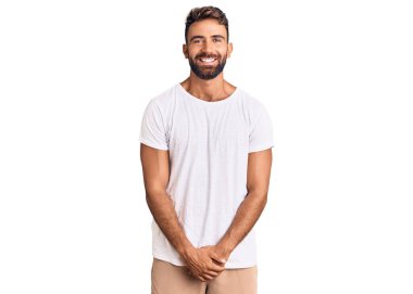 Yüzünde mutlu ve havalı bir gülümseme olan günlük beyaz tişört giyen genç bir İspanyol. şanslı kişi. 