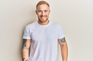 Yüzünde mutlu ve havalı bir gülümseme olan günlük beyaz tişört giyen genç beyaz bir adam. şanslı kişi. 