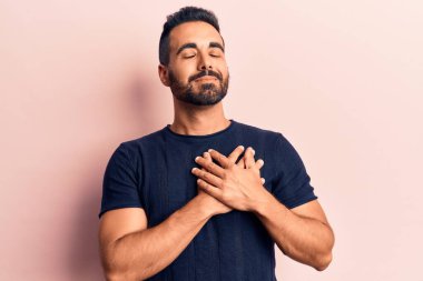 Gündelik kıyafetler giyen genç İspanyol adam elleri göğsünde gülümsüyor, gözleri kapalı ve yüzünde minnet ifadesi var. sağlık kavramı. 