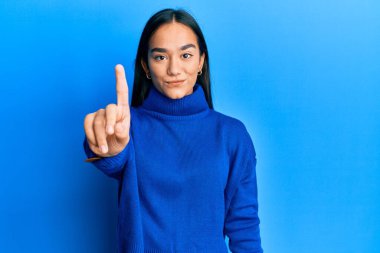 Kış süveteri giymiş genç Asyalı bir kadın parmağını kaldırmış ve kızgın bir ifadeyle işaret ediyor. Hiç hareket göstermiyor. 