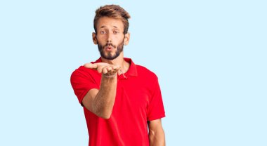 Sarışın, sakallı, sıradan kıyafetler giyen, kameraya bakıp havada öpüşen, güzel ve seksi bir adam. aşk ifadesi. 