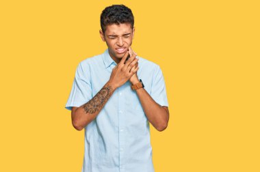 Genç ve yakışıklı Afro-Amerikan bir adam günlük kıyafetler giyip diş ağrısı ya da diş hastalığından dolayı ağızlarına acı dolu bir ifadeyle dokunuyor. dişçi 