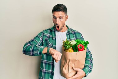 Sakallı yakışıklı bir adam elinde poşetle saatine bakıyor. Endişeli, geç kalmaktan korkuyor. 